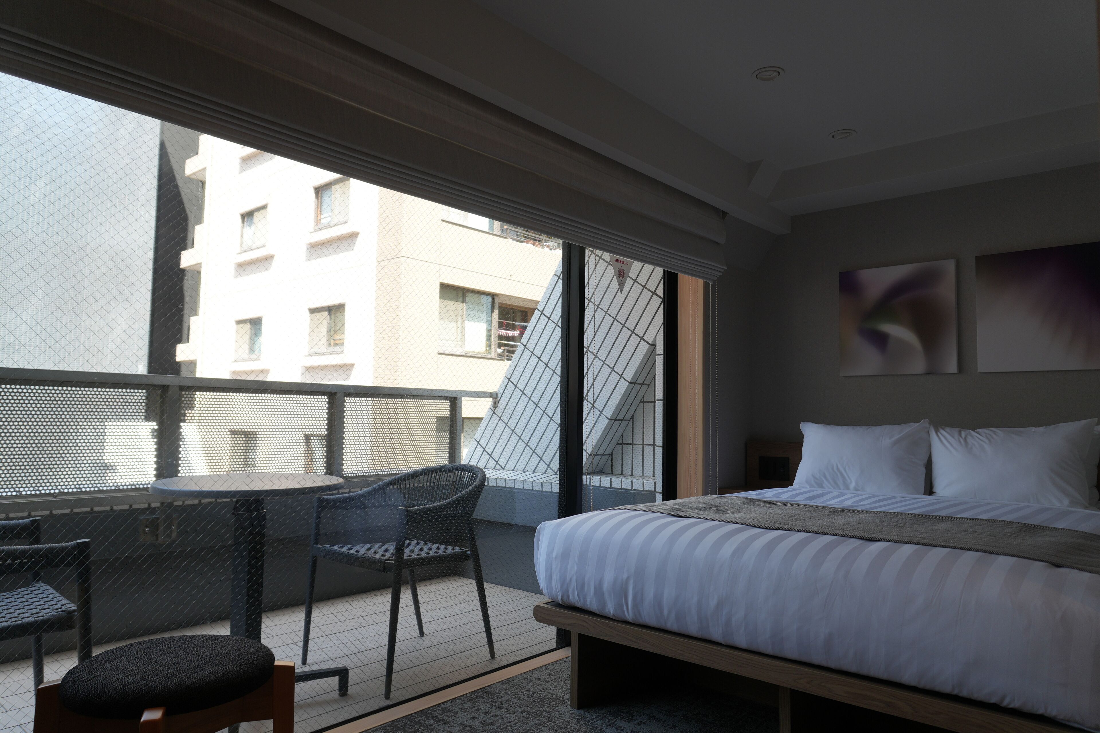 A hotel room with a bed, a small table with chairs, and a balcony with a view of buildings.