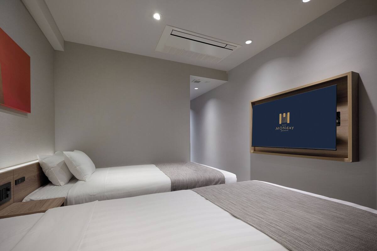 A hotel room with two beds, a mounted TV, and a red accent wall.