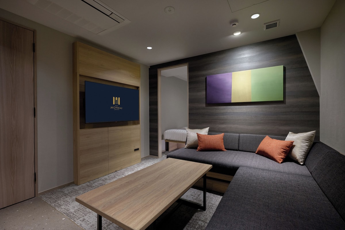 A modern hotel room with a sofa, a wooden table, and a wall-mounted TV displaying the hotel name.