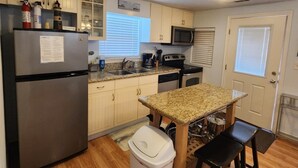 A compact kitchen with a refrigerator, microwave, sink, and a small dining area with stools.
