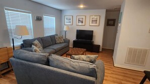 A modern living room with a sectional sofa, a flat-screen TV, and a ceiling light fixture.