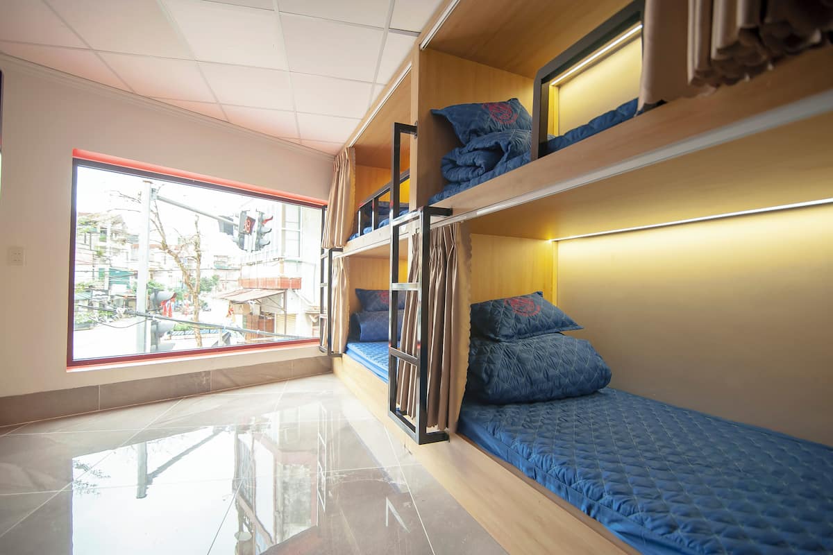 Une chambre de dortoir avec des lits superposés, une grande fenêtre et un sol carrelé.