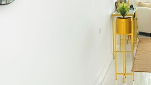 Un salon moderne avec un miroir rond, un téléviseur à écran plat, une petite table d’appoint jaune ornée d’une plante et un canapé beige.