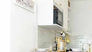 Une cuisine moderne avec des meubles blancs, un tabouret de bar noir et doré, et un panneau sur lequel on peut lire : « Savourez chaque instant. »