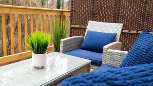 Un espace extérieur aménagé avec des meubles en osier, une table en verre, des coussins bleus et une plante en pot.
