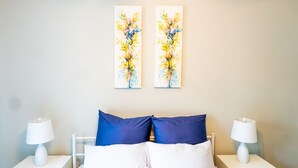 Une chambre d’hôtel avec un lit, deux oreillers bleus, du linge de lit blanc, deux tables de chevet avec des lampes et deux tableaux accrochés au mur.