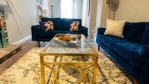 Un salon avec un canapé bleu, une table basse en verre et un tapis à motifs.