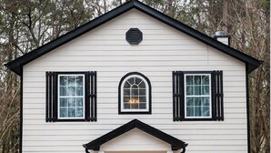 Une maison blanche à deux étages, avec des volets noirs, une fenêtre en arc de cercle au centre et un porche à l’avant.