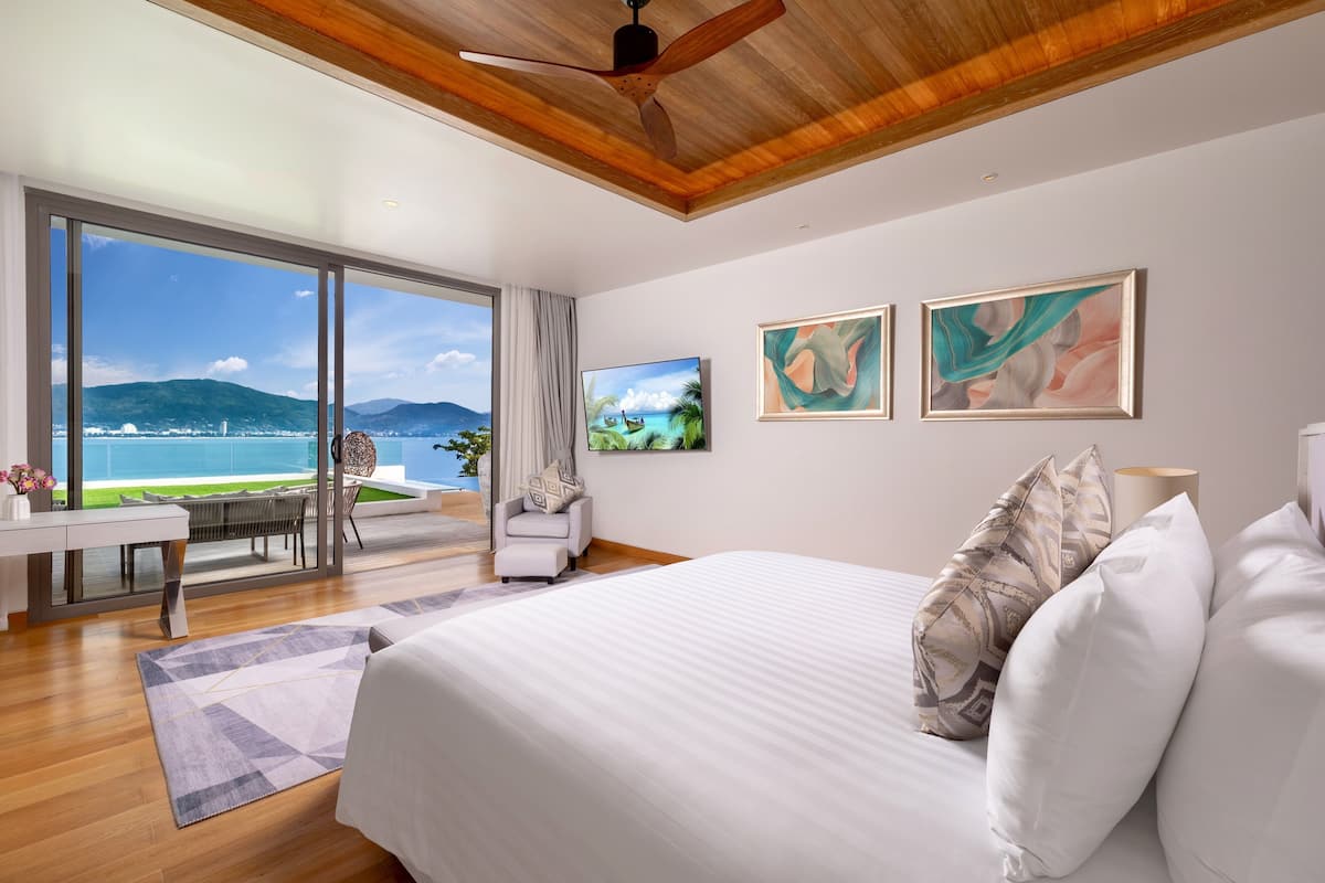 A modern bedroom with a large bed, a desk, and a view of the sea.