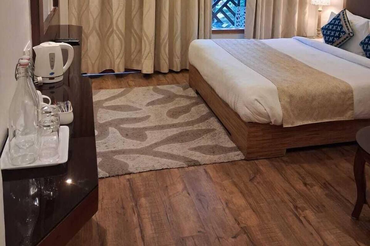 A hotel room with a bed, a desk with a coffee maker, a window with curtains, and a view of a balcony.