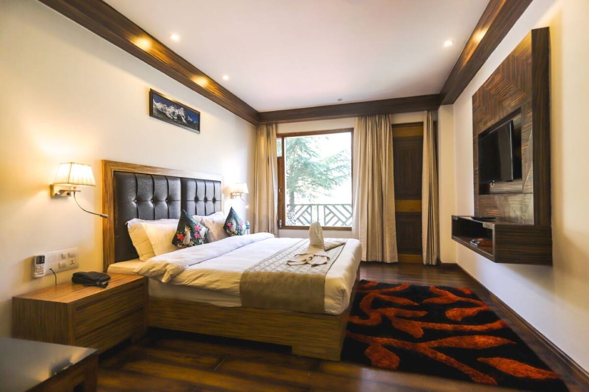 A hotel room with a bed, bedside table, lamp, and a TV mounted on the wall.