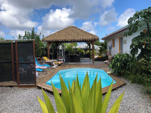 A backyard with a wooden deck, a swimming pool, a thatched-roof gazebo, and various plants. - Villa Kaz à Colibri with swimming pool for a relaxing break with family or friends (Unknown)