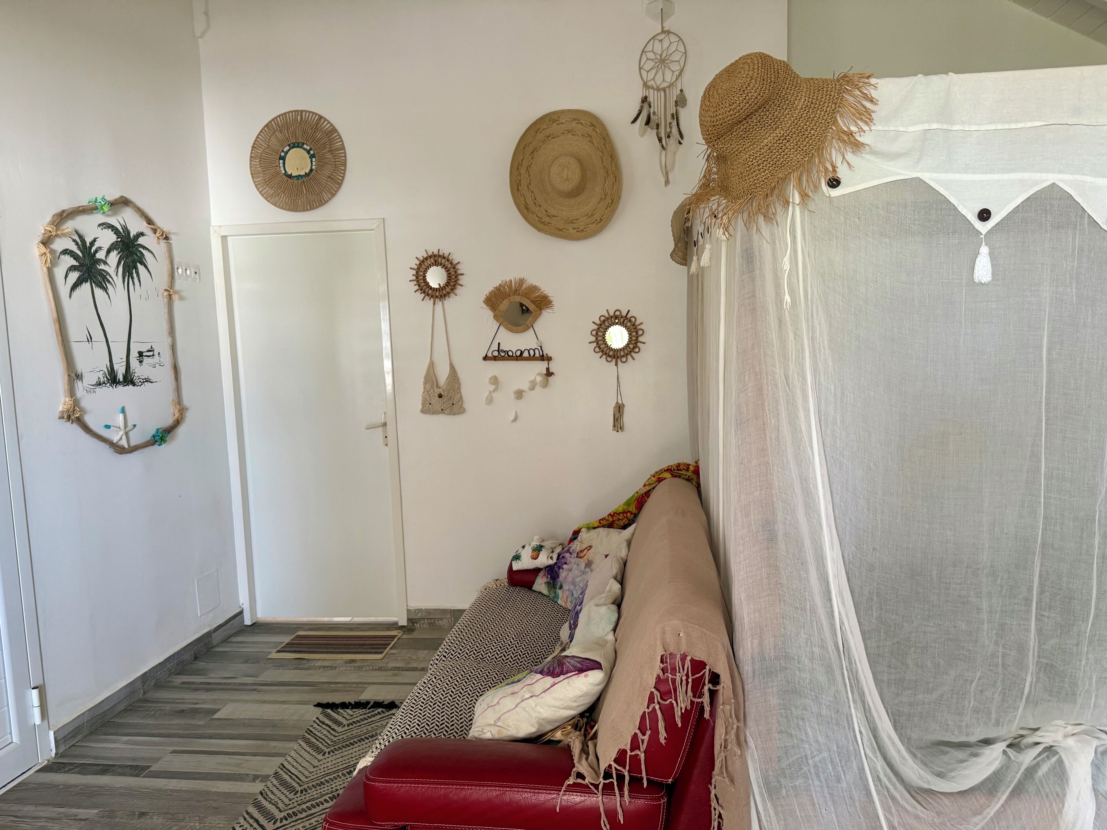 A room with a patterned floor, a red sofa, a white door, and wall decorations including dream catchers and a mirror.
