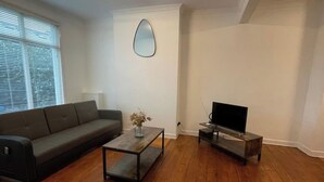 A living room with a sofa, a coffee table, a TV on a stand, and a mirror on the wall.