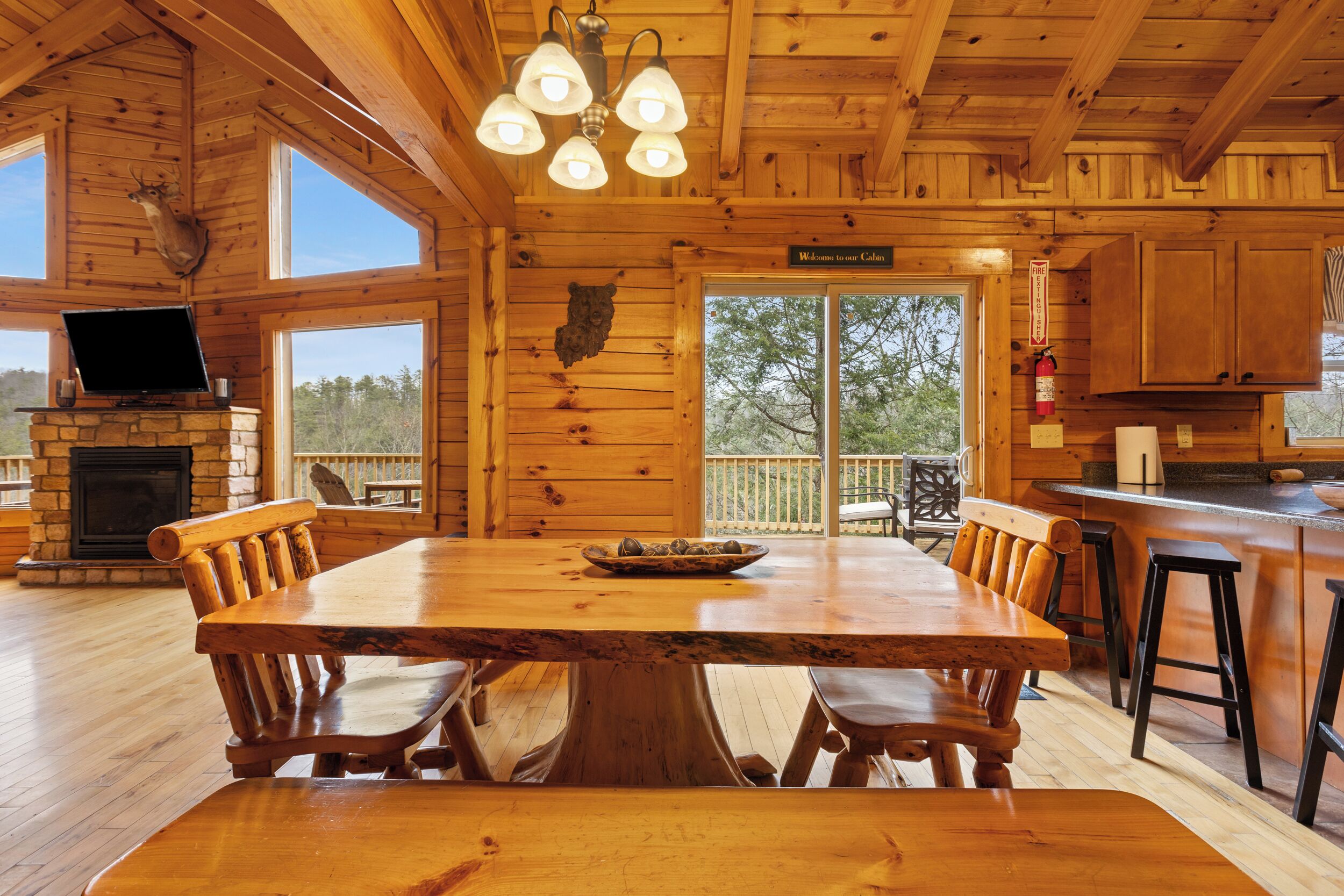 L’intérieur d’un chalet en bois comprend une grande table à manger, des bancs en bois, une cheminée en pierre et un téléviseur.
