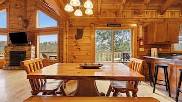 L’intérieur d’un chalet en bois comprend une grande table à manger, des bancs en bois, une cheminée en pierre et un téléviseur.