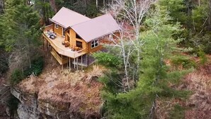 Una cabaña de madera con terraza, rodeada de bosque y ubicada sobre un acantilado.