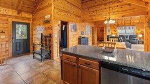Interior de una cabaña de madera con cocina que incluye encimeras de granito, lavavajillas y armarios de madera.
