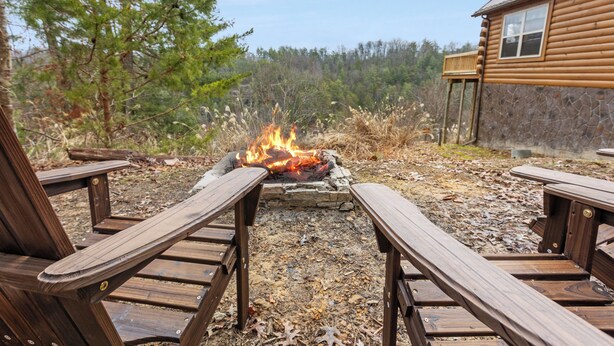 Una terraza de madera con dos sillas frente a un pozo de fuego de piedra.