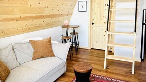 A cozy room with a wooden sloped ceiling, a sofa, two stools, a ladder, and a patterned rug. - `The Scout`: a cozy mountain cabin with million dollar view (Ironton)