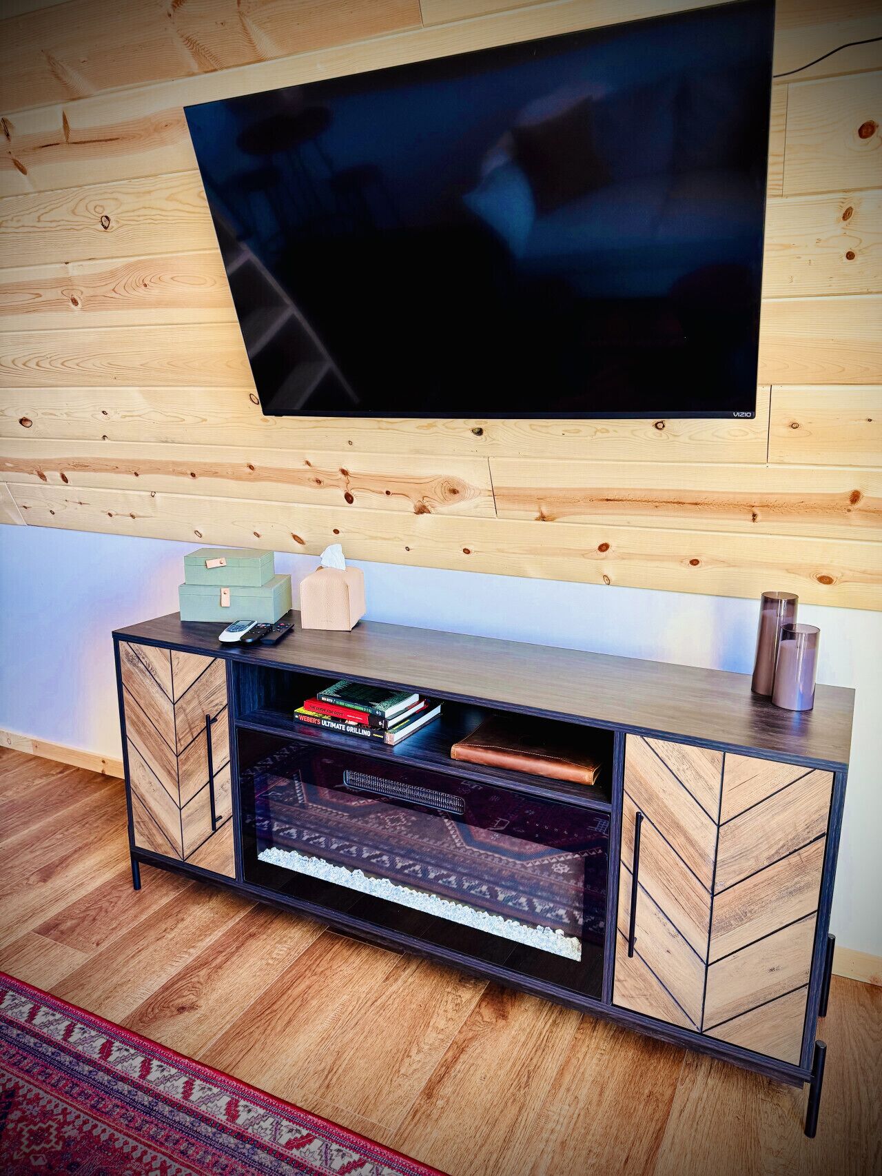 Un salon moderne avec un téléviseur fixé au mur, un meuble en bois rempli de livres et un tapis à motifs.