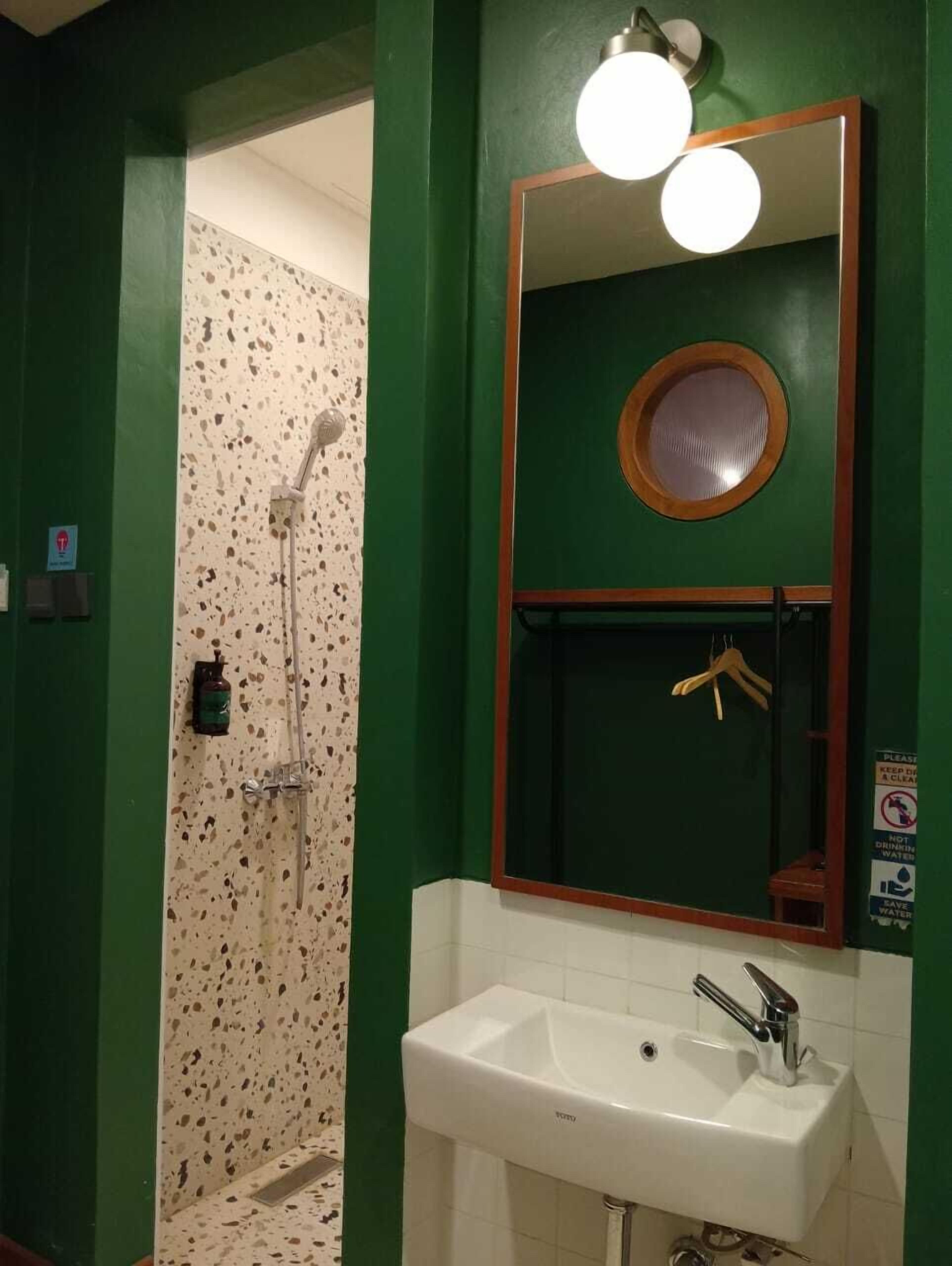 Un baño con pared verde, un lavabo blanco, un espejo con marco de madera y una ducha con pared de azulejos con motas.