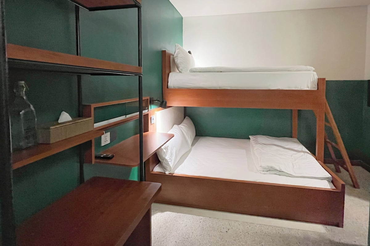 A bunk bed room with a wooden desk and shelves, a bottle, and a lamp.