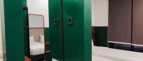 A hotel room with a green accent wall, a white sink, a mirror, a bed, and a wardrobe.