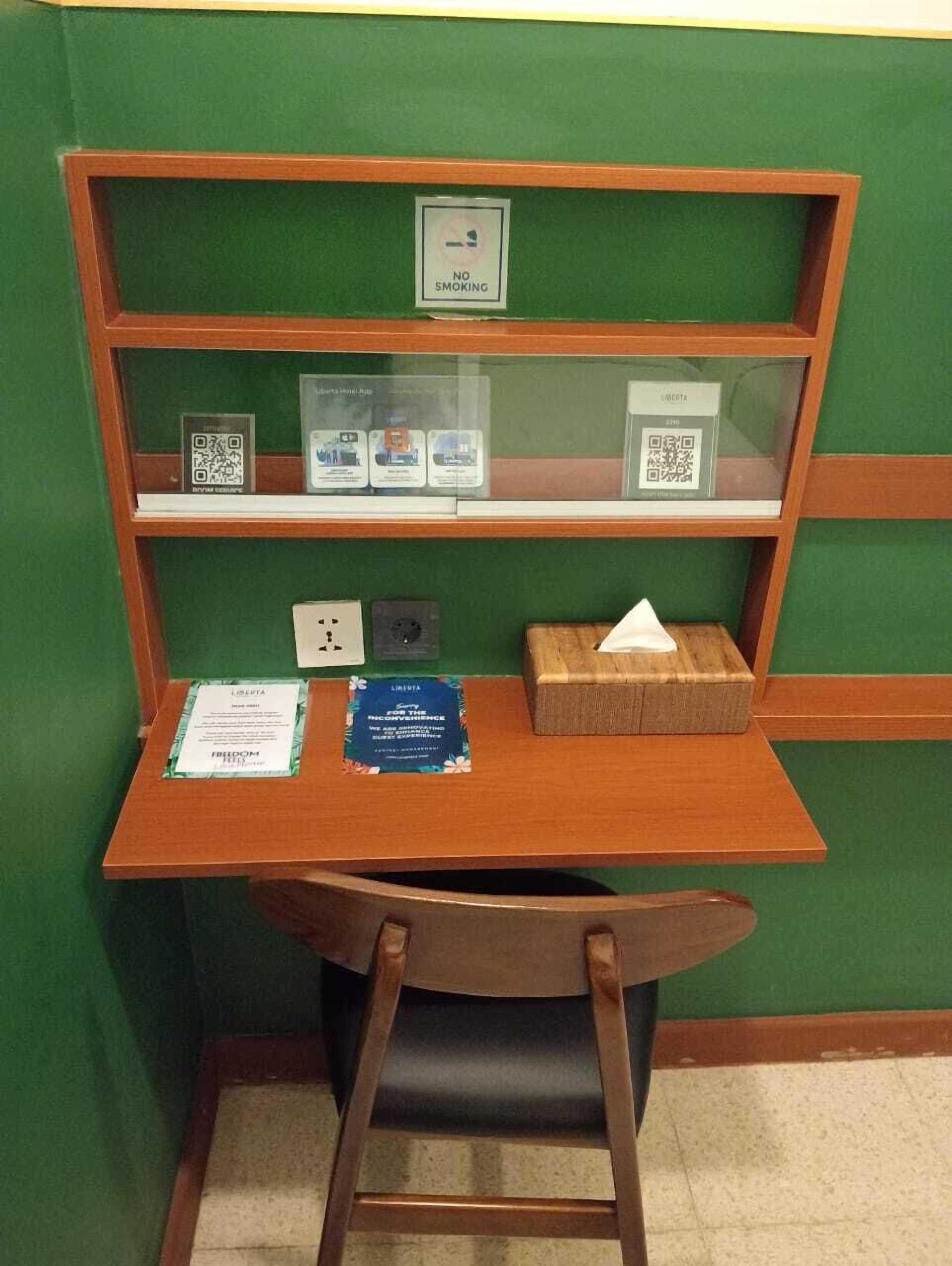 A small wooden desk with a chair, a sign prohibiting smoking, and informational brochures.