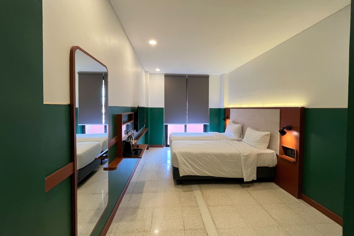 A hotel room with two beds, a large mirror, a desk with a chair, and a small table.