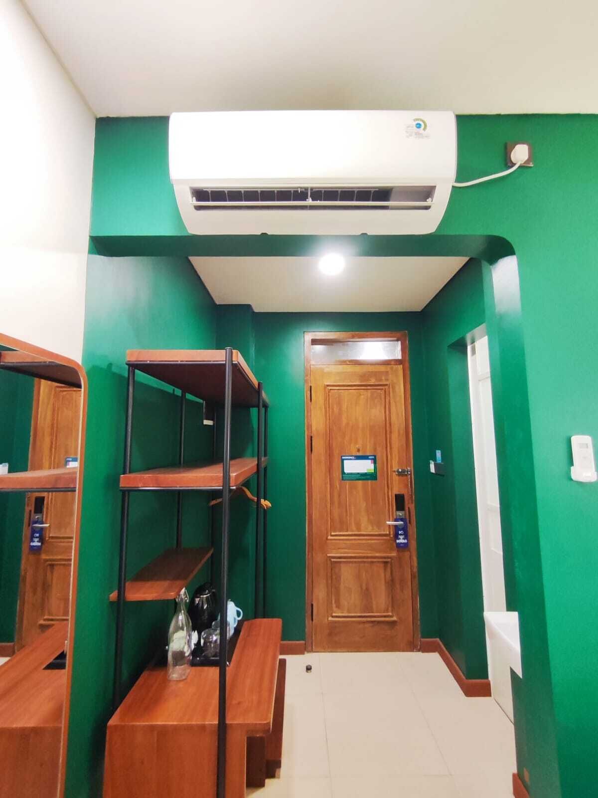 A room with green walls, a wooden door, a bench, a shelf unit, and an air conditioning unit.