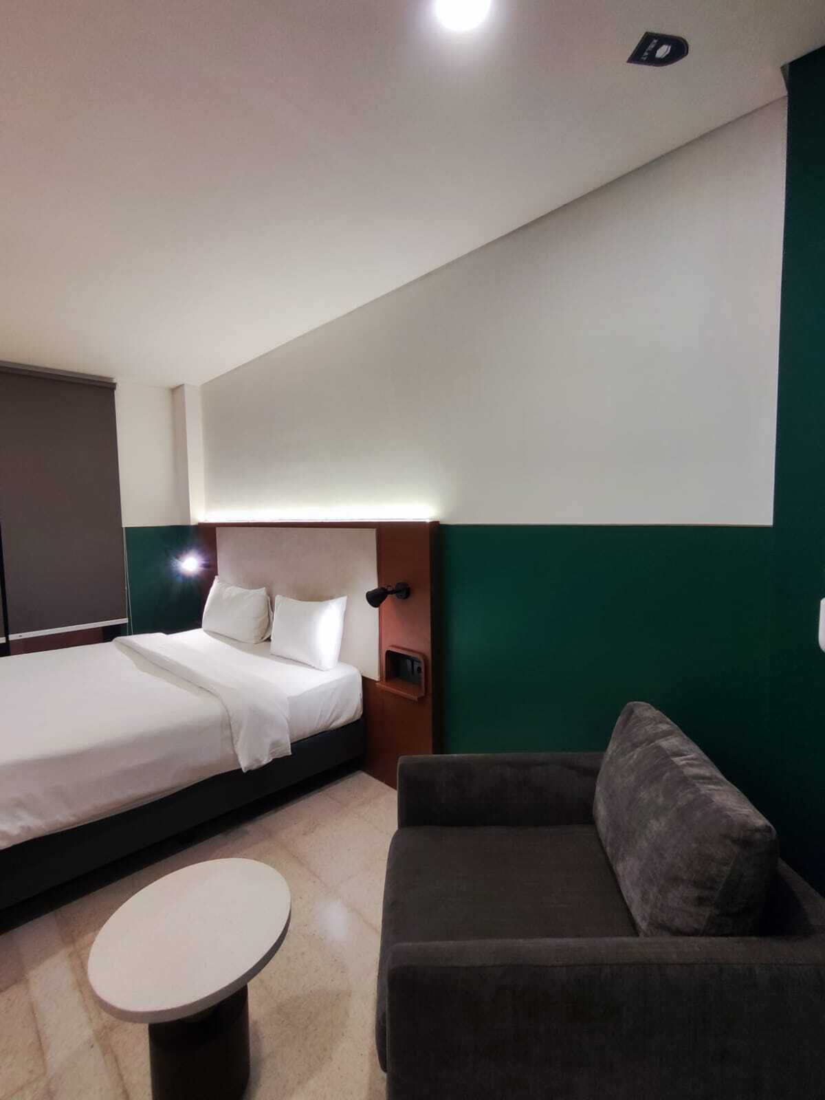 Una habitación de hotel con cama, sofá, una mesita y una lámpara en la pared.