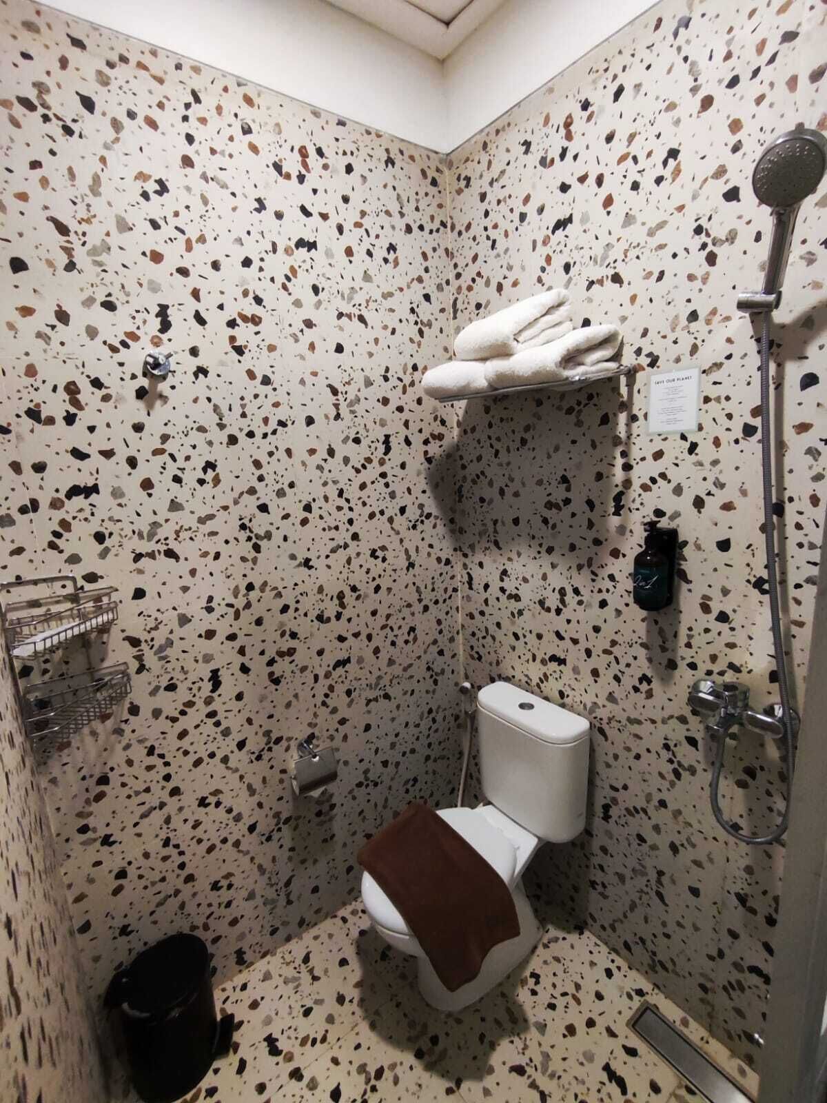 A small bathroom with a speckled tile wall, a toilet, a shower, and a towel rack.