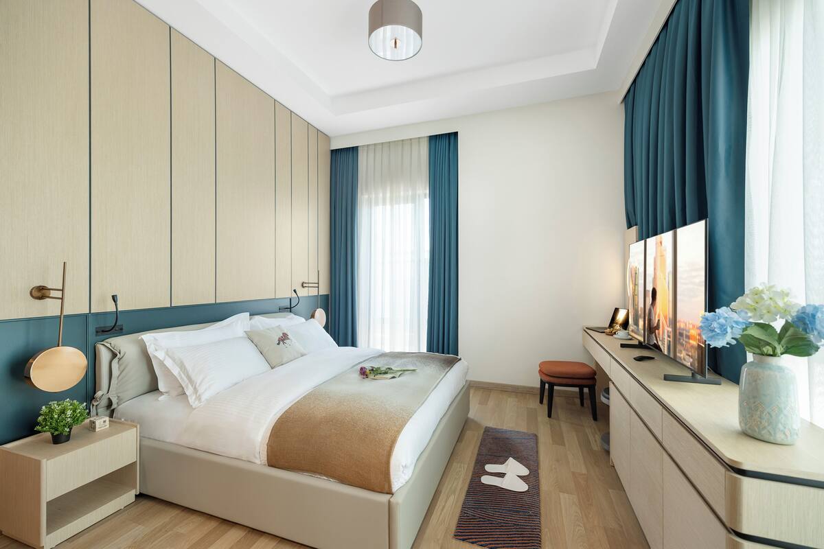Ein modernes Hotelzimmer mit einem großen Bett, Nachttischen, einem Schreibtisch und Blick auf die Stadt.