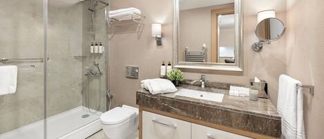 A modern bathroom with a glass-enclosed shower, a white toilet, a marble sink, and a large mirror.