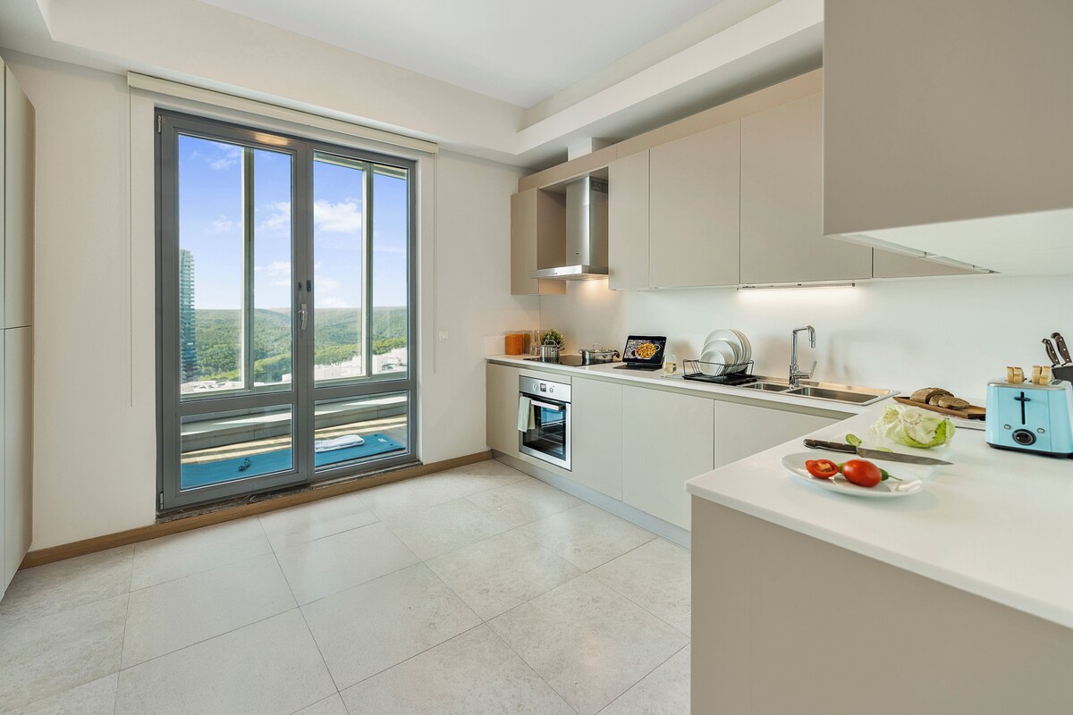 A modern kitchen with a large sliding glass door leading to a balcony, a built-in oven, and a white countertop with a toaster and vegetables.