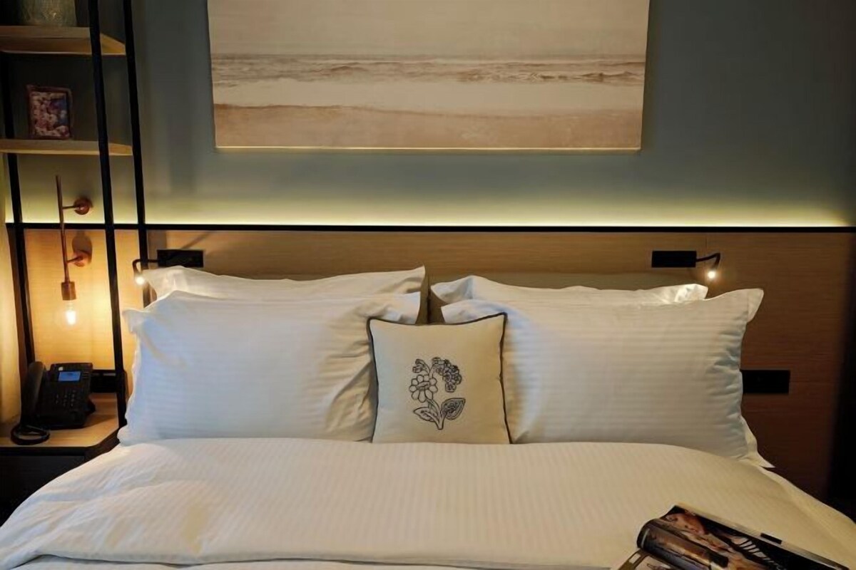 A neatly made bed with white linens, a decorative pillow, and a bedside table with a phone.