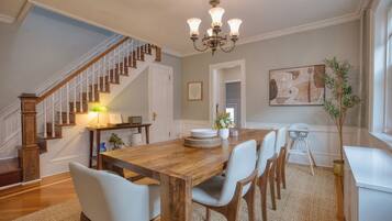 A dining area with a wooden table, white chairs, a chandelier, and a staircase.