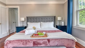 Una camera da letto con un letto grande, due comodini, un tavolino, una finestra con tende e una porta che conduce a un'altra stanza.