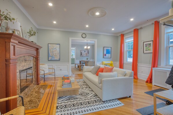A living room with a fireplace, sofa, coffee table, and a view of the dining area. - Near Prospect Park, Comfy King Beds, Nice Outdoor Space, Free Parking EV Charger (Brooklyn)