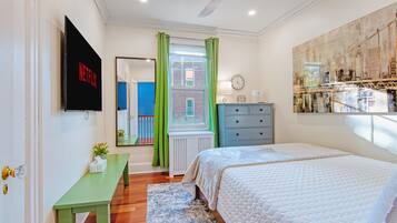 A bedroom with a bed, a dresser, a TV mounted on the wall, a window with green curtains, and a radiator.