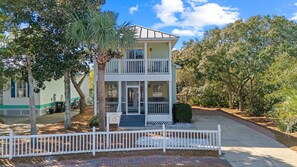 A two-story building with a balcony, a sign indicating it is a historic house, and a white picket fence in front.