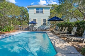 A swimming pool with lounge chairs and umbrellas, surrounded by a wooden fence and trees. - Charming house in delightful Destin with pool, AC, WiFi, private beach access (Destin)