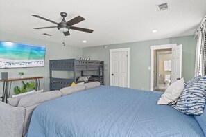 A bedroom with a bunk bed, a ceiling fan, a flat-screen TV, and a large bed with blue bedding. - Charming house in delightful Destin with pool, AC, WiFi, private beach access (Destin)