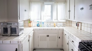 A compact kitchen with white cabinets, a built-in oven, a stove, and a window with curtains.