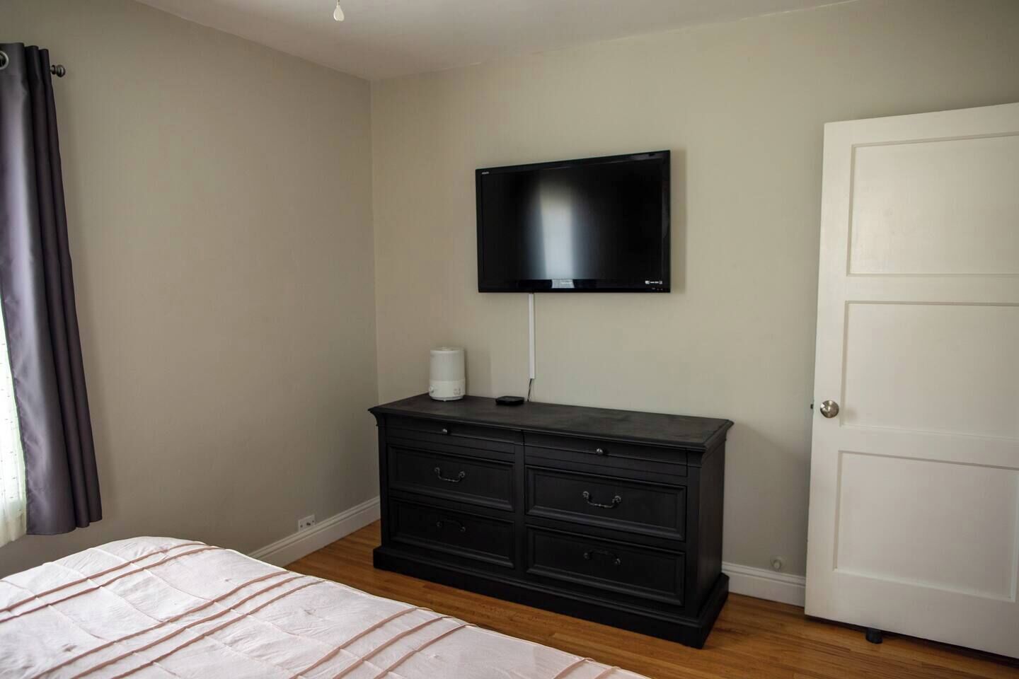 Een slaapkamer met een bed, een dressoir, een aan de muur bevestigde televisie en een deur.