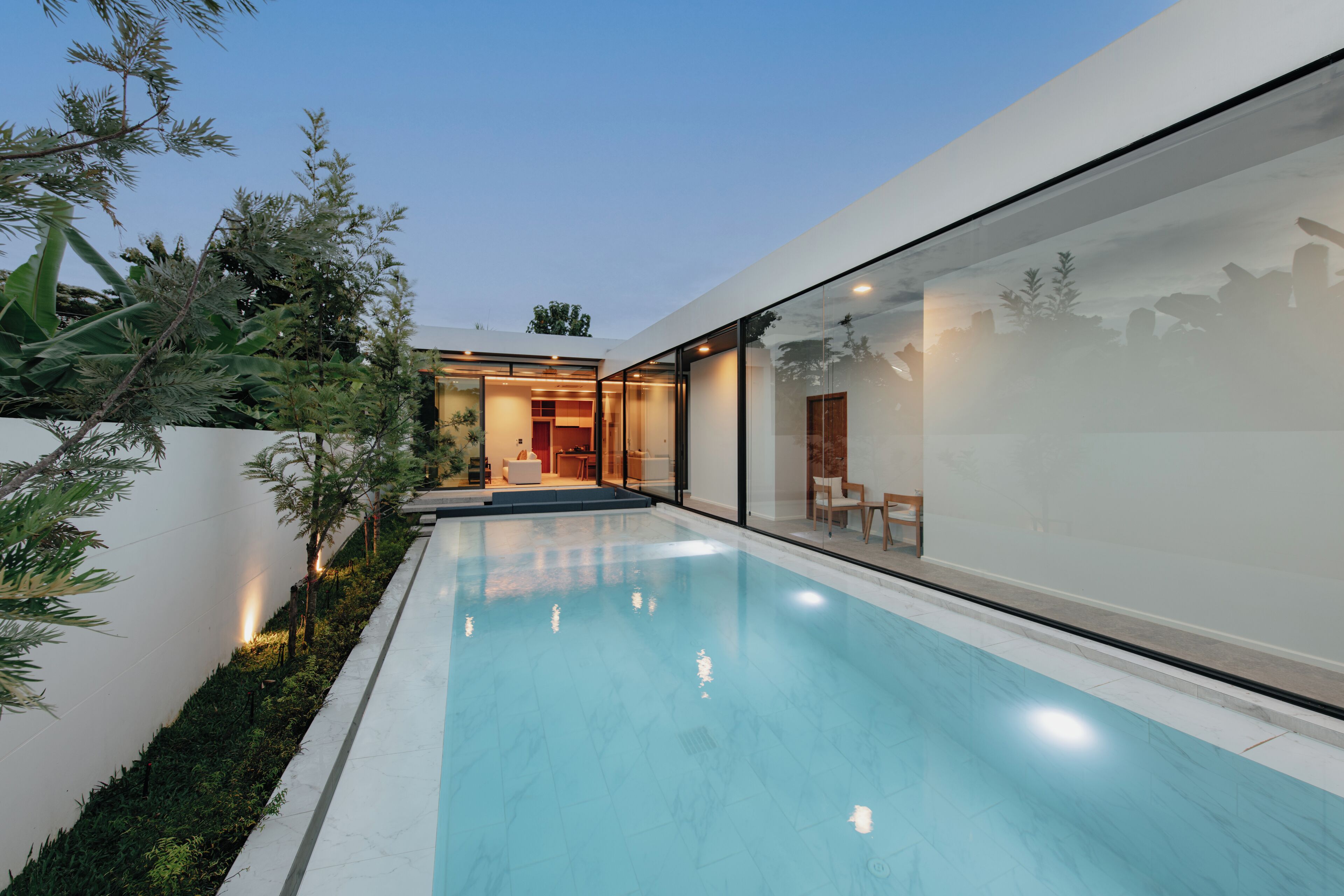 Una casa moderna con piscina, paredes de vidrio y un interior bien iluminado.