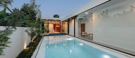 Una casa moderna con piscina, paredes de vidrio y un interior bien iluminado.