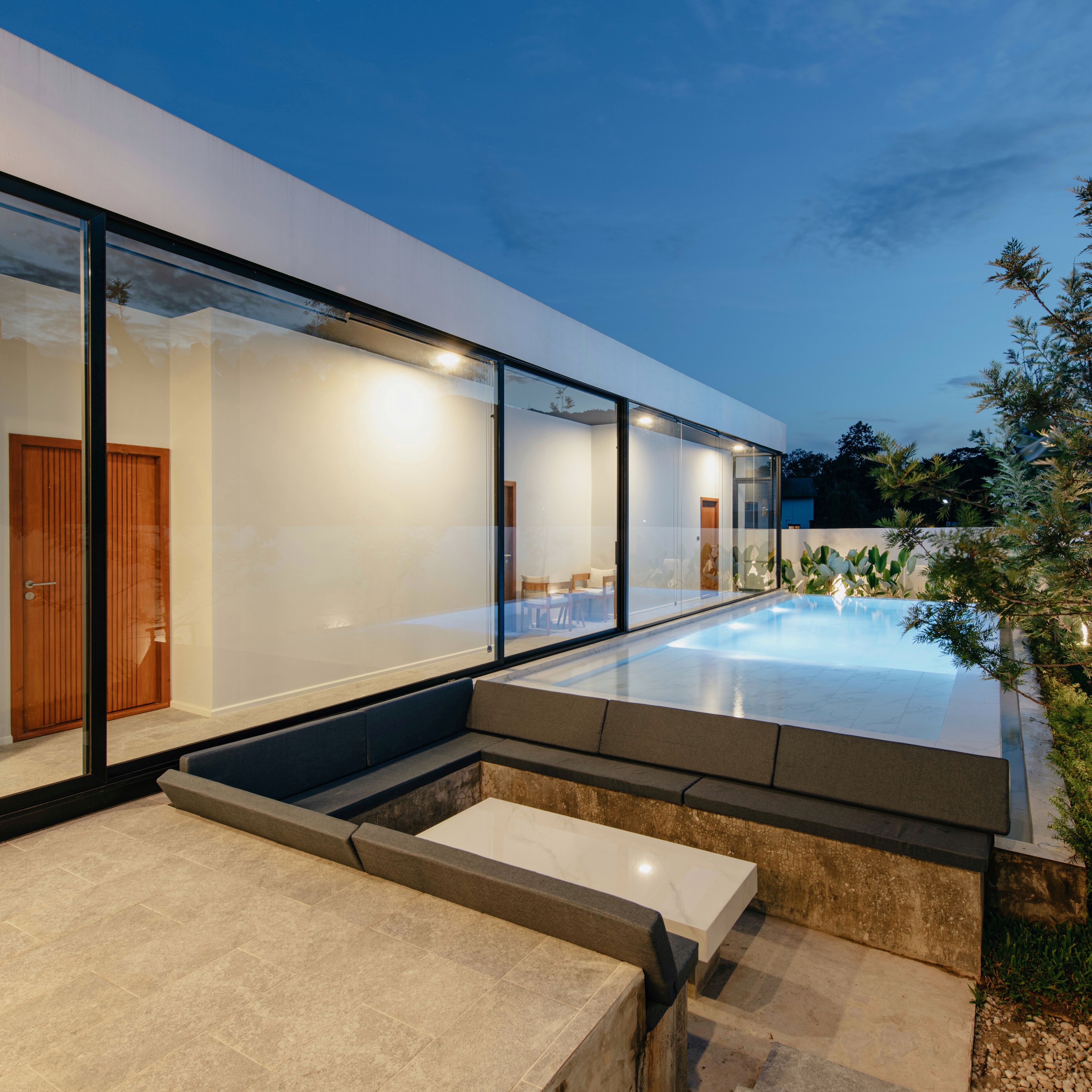 A modern house with a glass facade, a swimming pool, and a patio area.