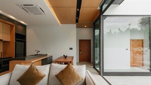 A modern kitchen with a built-in oven, a dining area with a table and chairs, and a large glass door leading to a patio. - TUL VIlla Chiangmai (Chiang Mai)